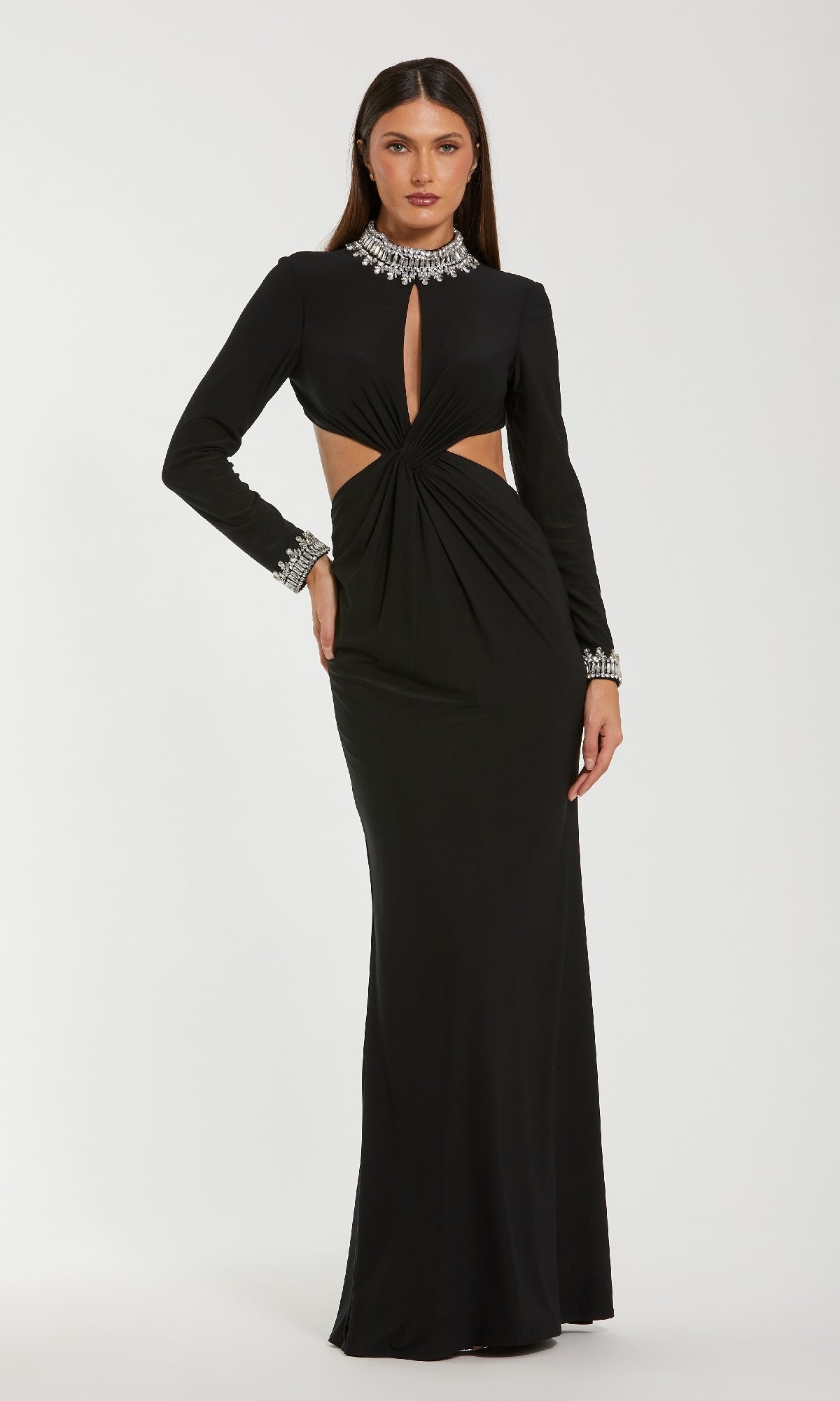 A woman models the Mac Duggal 44155 long formal dress—black jersey with a jeweled collar and cuffs, front keyhole cutout, and gathered waist cutouts—posed against a plain light background.